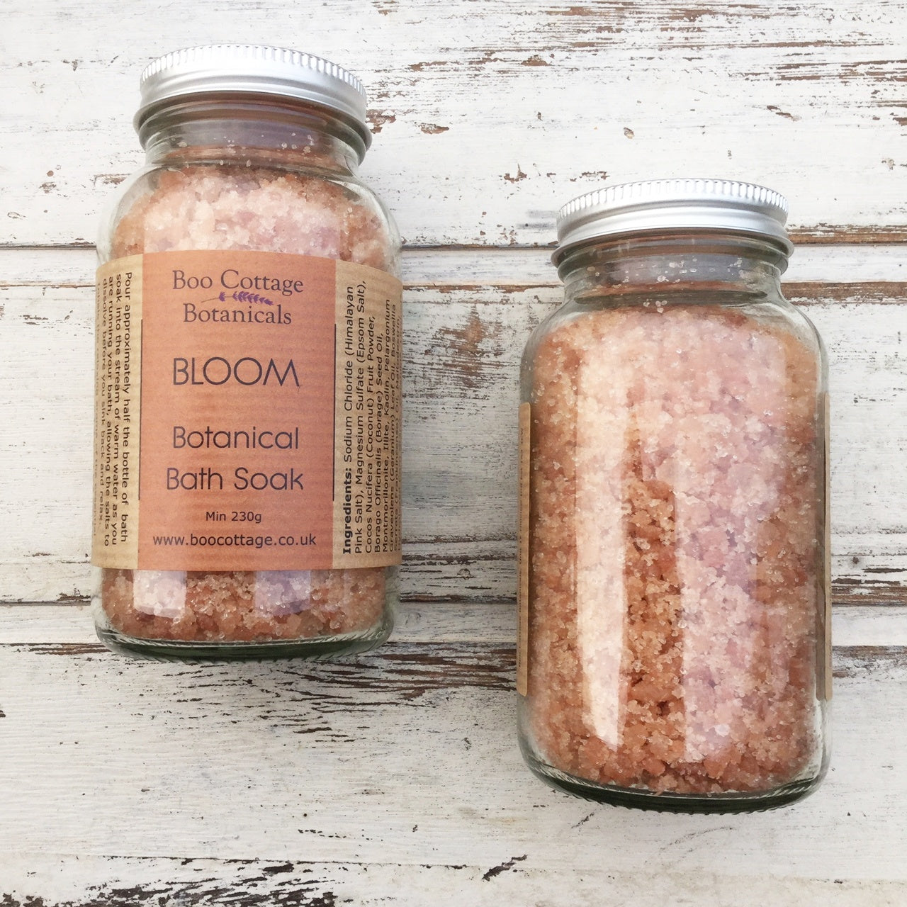 Pink BLOOM bath salts in clear bottles on whitewashed wooden background