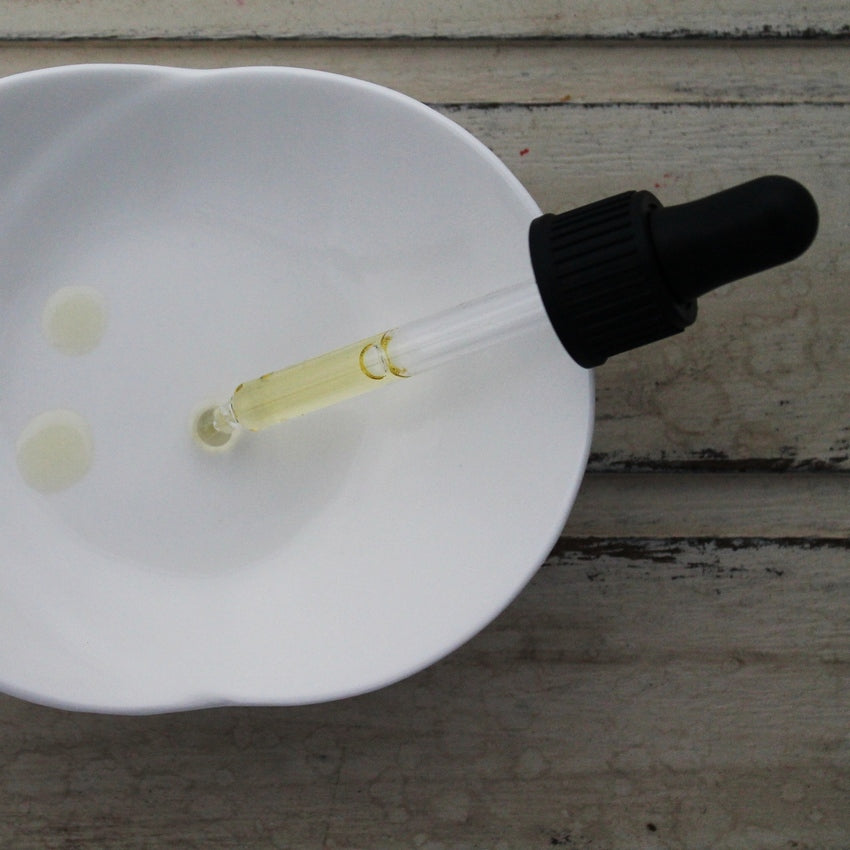 Balance face oil pipette with black dropper dropping oil into white dish