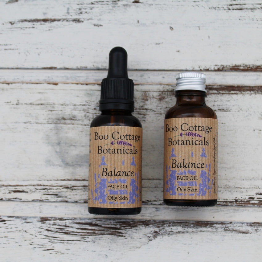 Amber bottles of Balance Face Oils, one with black dropper pipette, one with aluminium lid on whitewashed wooden background
