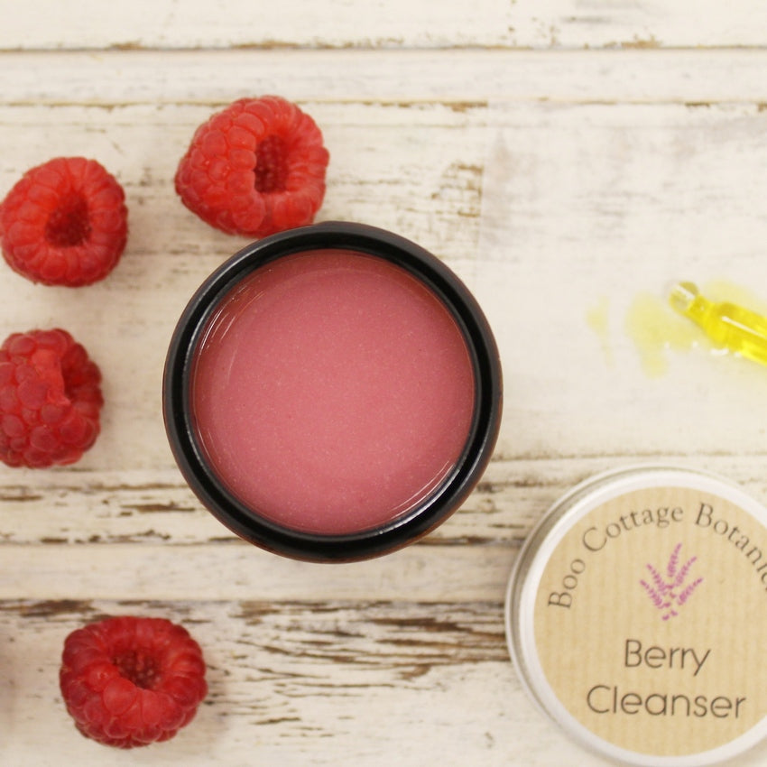 Pink balm in amber jar from above with lid and raspberries on whitewashed background