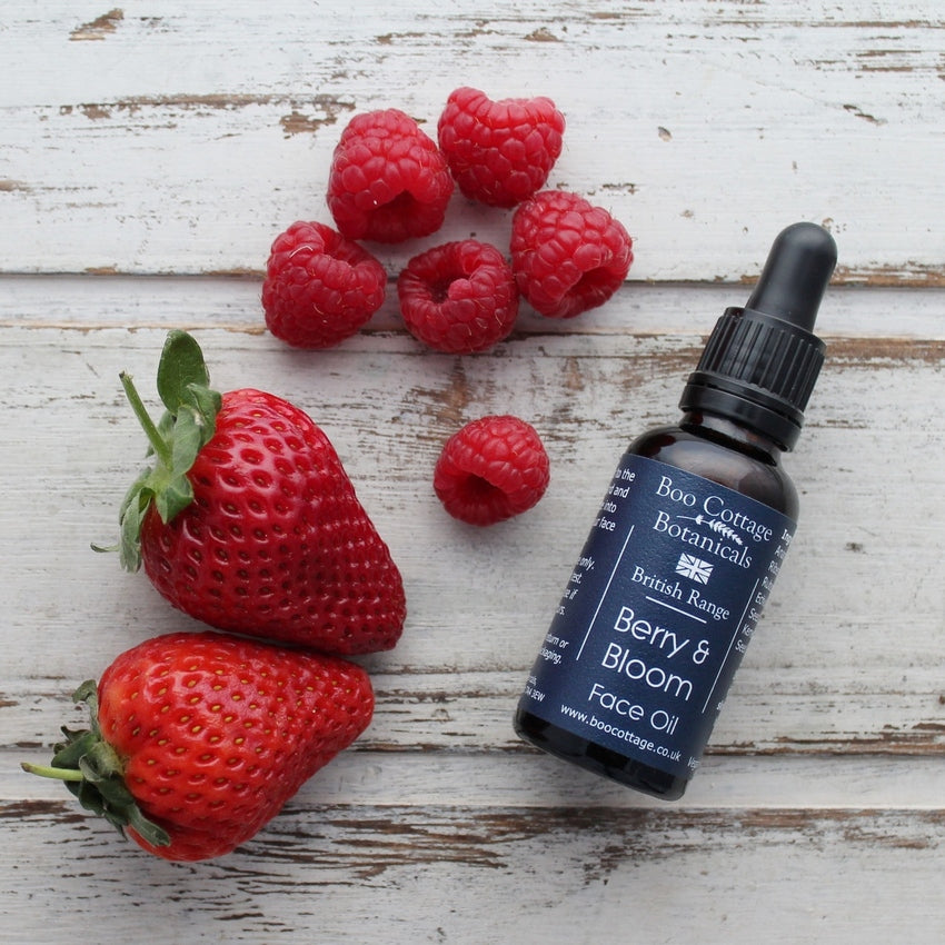 Berry & Bloom Face oil in amber bottle with black dropper pipette on whitewashed wooden background with strawberries and raspberries