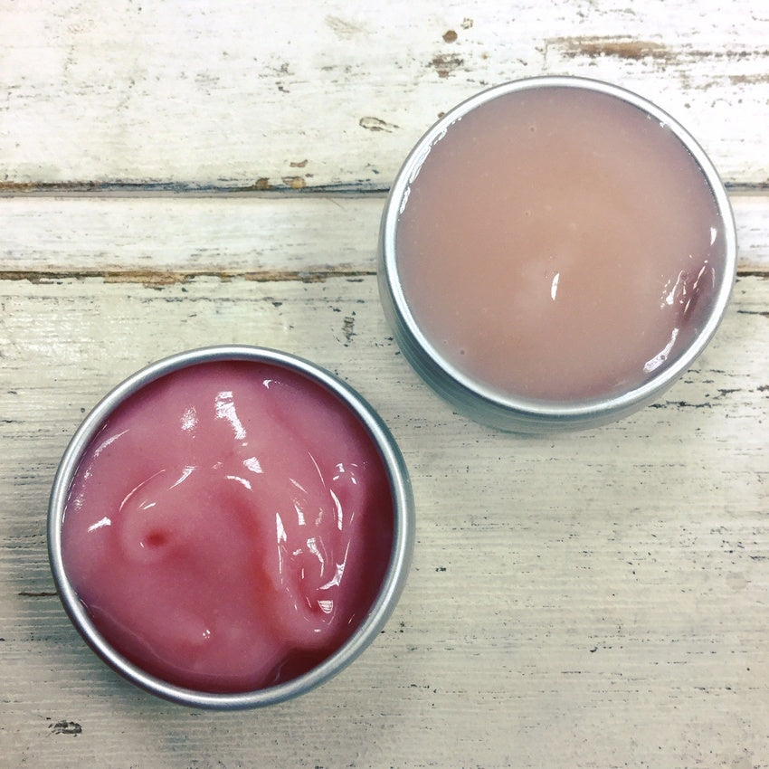 Mini aluminium tins of berry cleanser showing difference in colour between bright and pale pink on white washed wooden background