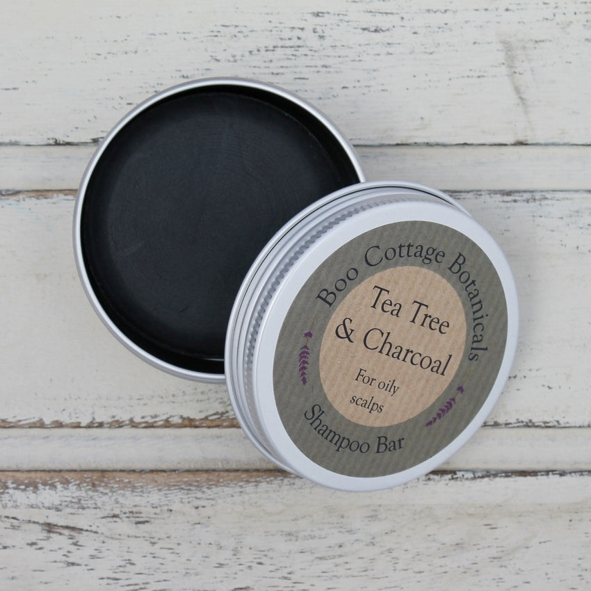 Open round aluminium tin showing black shampoo bar inside on whitewashed wooden background