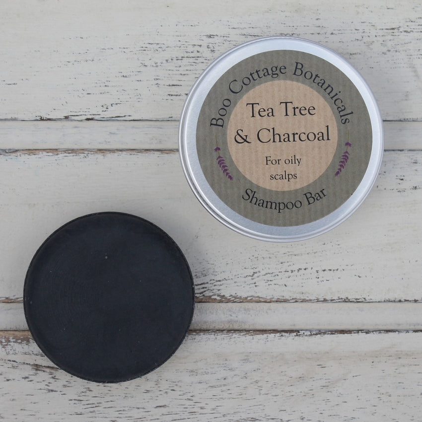 Unwrapped black round flat shampoo bar and round aluminium tin with grey label on whitewashed wooden background