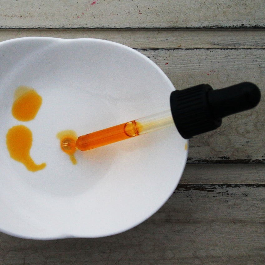 Orange face oil in black dropper pipette dropping oil into white dish