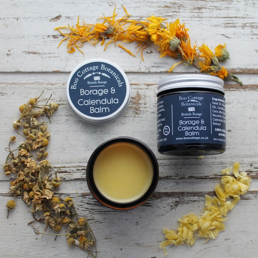 Open and shut jar of yellow balm on whitewashed background with beeswax, calendula and chamomile flowers