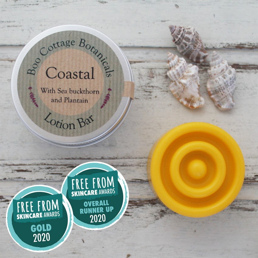 Yellow round solid lotion bar with round tin on whitewashed wooden background with sea shells and Free From Skincare Awards badges