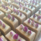 Bars of handmade pink soap with rose bud toppings stood together in rows