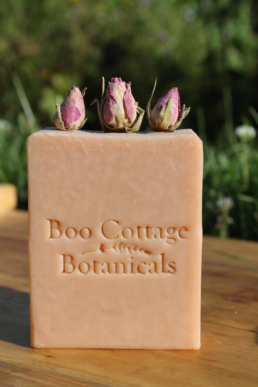 Pink soap bar with rose buds on top on wooden table with green outdoor background