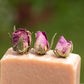 Close up of top of pink soap bar with 3 dried rose buds in the top against green outdoor background