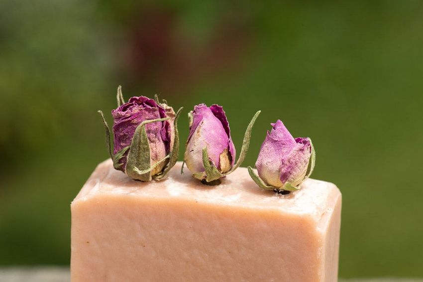 Close up of top of pink soap bar with 3 dried rose buds in the top against green outdoor background