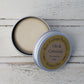 Open round aluminium tin with cream shampoo bar inside on whitewashed wooden background