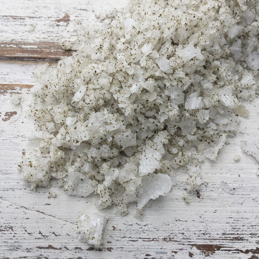Close up of white sea salt with green flecks of seaweed on a whitewashed wooden background