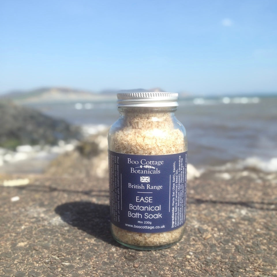EASE bath soak in glass bottle with navy blue label on wall in front of sea with blue sky