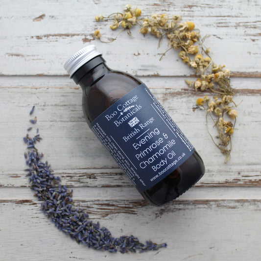 Body oil in amber bottle with aluminium lid and navy blue label on whitewashed wooden background with lavender and chamomile flowers