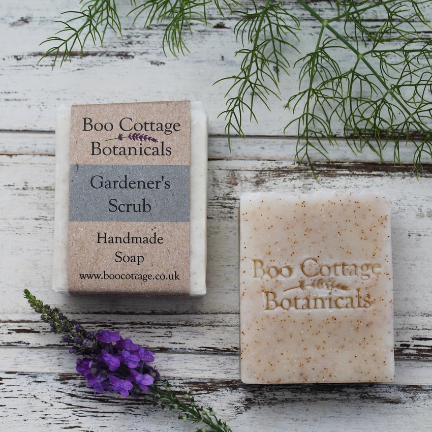 Wrapped and unwrapped speckled white soap bar on whitewashed wooden background with fennel and purple flower