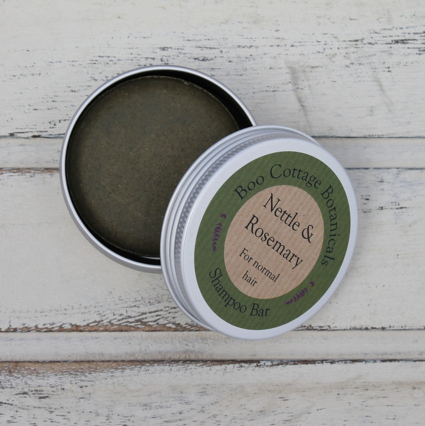 Open round aluminium tin with green label showing dark green shampoo bar inside on whitewashed wooden background