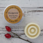 Cream circular solid lotion bar with round texture and aluminium tin on whitewashed background with rosehips 