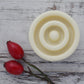 Close up view of cream round solid lotion bar with groved texture and red rosehips on whitewashed background