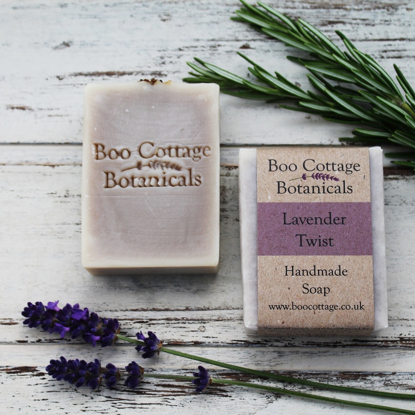 Unwrapped and wrapped pale grey-purple soap bar with fresh rosemary and lavender on whitewashed wooden background