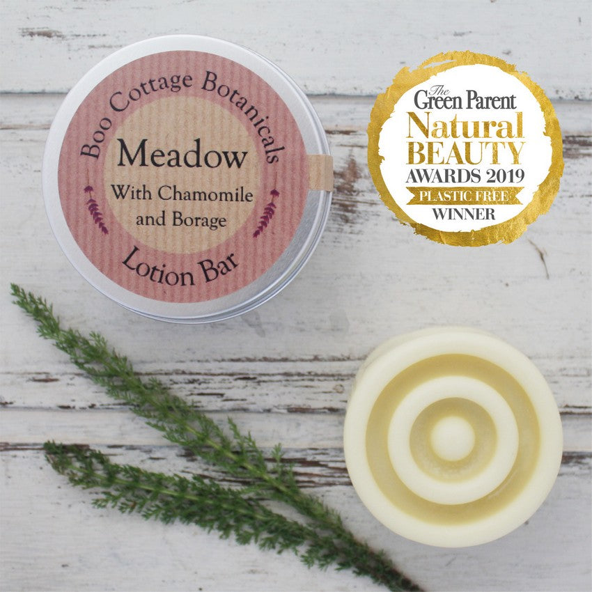 Round cream solid lotion bar with round tin on whitewashed wooden background with yarrow leaves and Green Parent Awards Badge