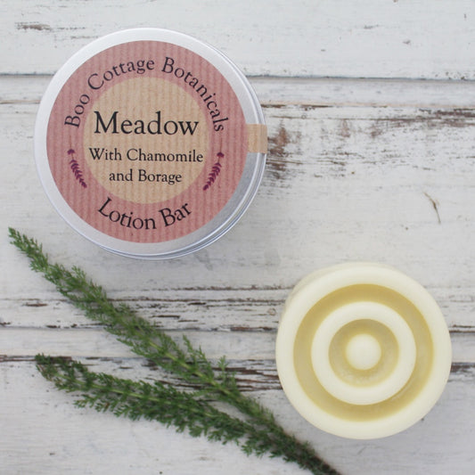 Cream round solid lotion bar with circular tin on whitewashed background with yarrow leaves