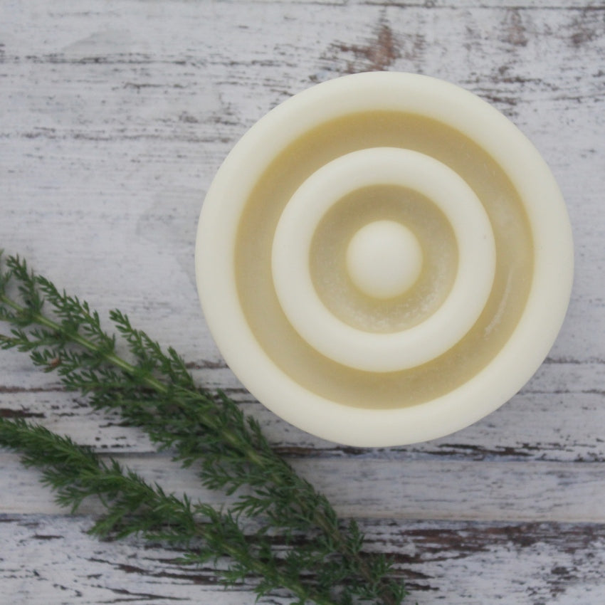 Close up of circular lotion bar with round groves on whitewashed wooden background with yarrow leaves