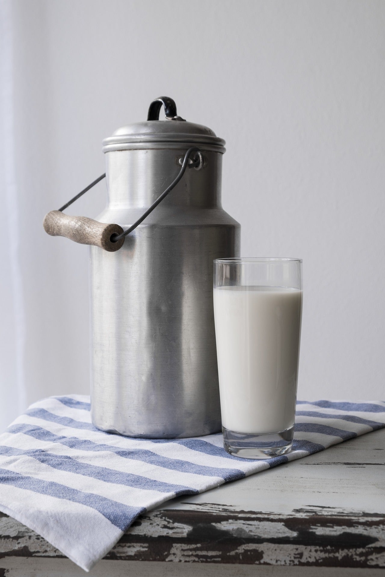 Vintage aluminium milk carrier and glass of milk on striped cloth with white background