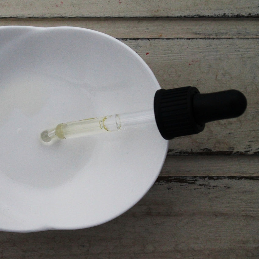 Clear oil in pipette with black dropper dropping oil into white dish