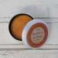 Open aluminium round tin with orange shampoo bar inside on whitewashed wooden background