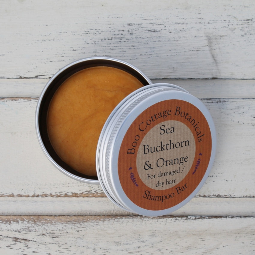 Open aluminium round tin with orange shampoo bar inside on whitewashed wooden background