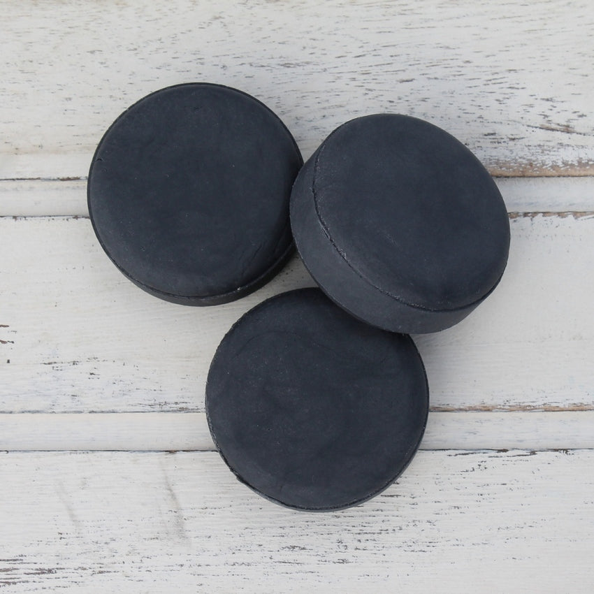 Pile of three flat round black shampoo bars on whitewashed wooden background