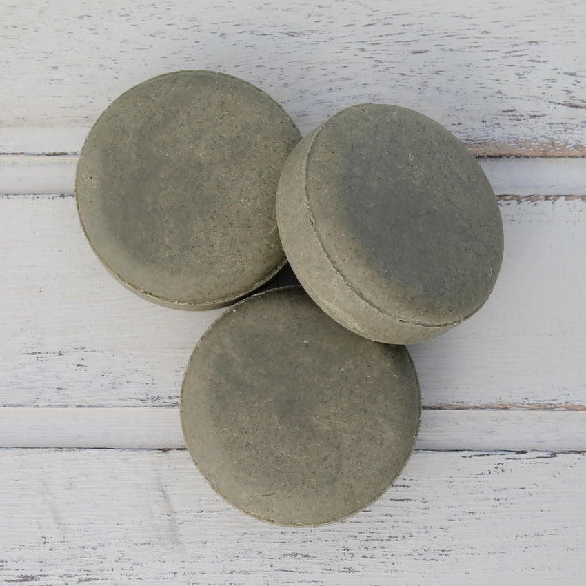 Pile of 3 dark green flat round shampoo bars on whitewashed wooden background