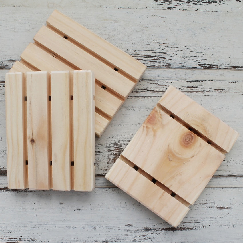 Pale wooden soap dishes with water draining grooves on whitewashed wooden background