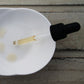 Pale oil in pipette with black dropper dropping oil into white dish