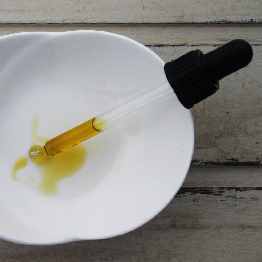 Greenish-yellow oil in black lidded dropper pipette dropping oil into white dish